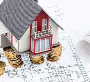 7 Schritte zum Glück: Online-Baufinanzierungsrechner Haus auf Münzen und Grundriss - Symbolbild Fertighaus-Baufinanzierung